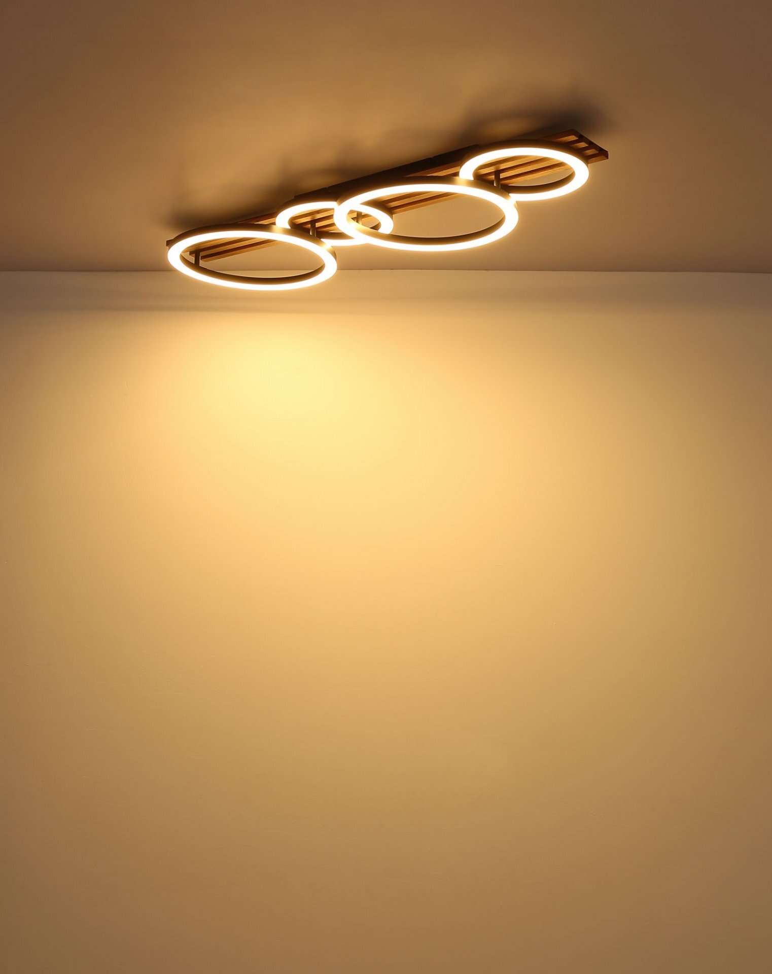 Na suficie zamontowana jest nowoczesna lampa sufitowa LED z czterema okrągłymi elementami świetlnymi, emitująca ciepłe, żółte światło. Ściana poniżej jest oświetlona miękkim blaskiem lampy.