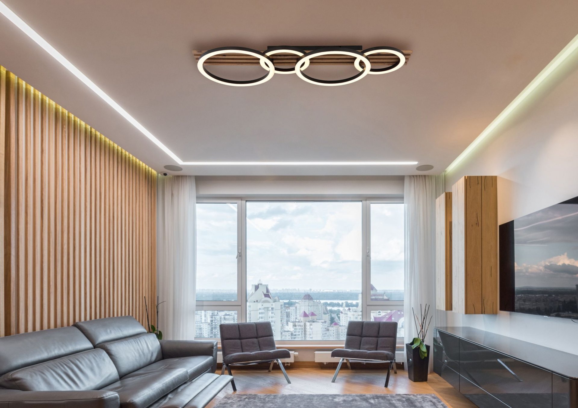 Nowoczesny salon z dużym oknem, skórzaną sofą i dwoma fotelami. Na suficie zamontowana jest lampa sufitowa z kilkoma okrągłymi elementami LED.