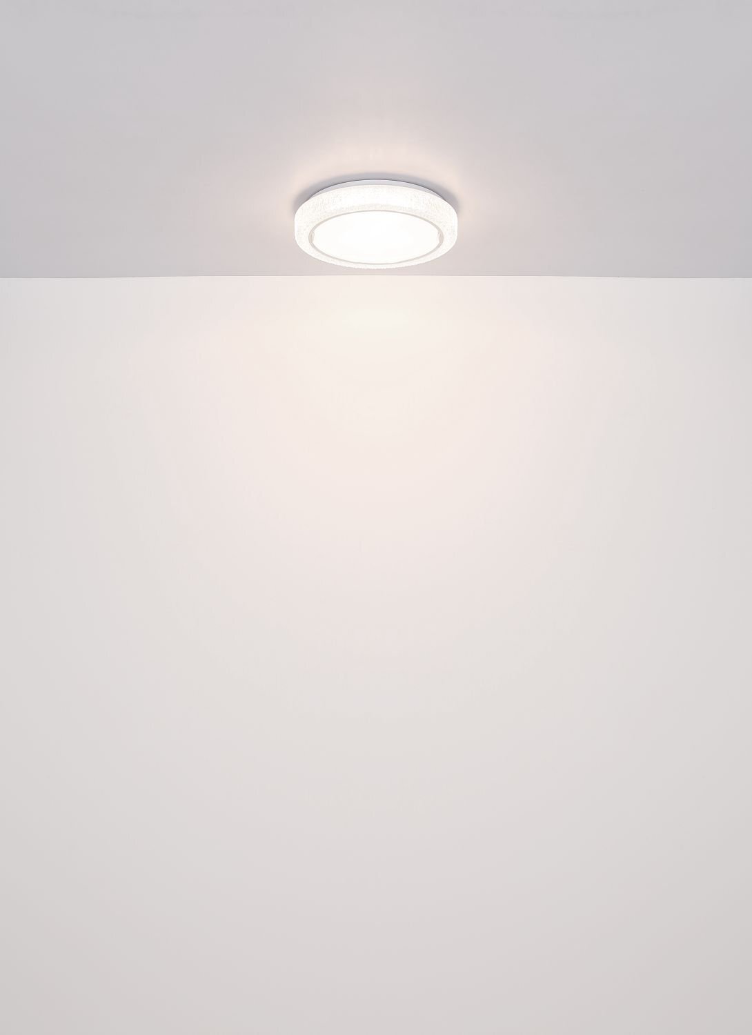 Na obrazie widoczna jest nowoczesna lampa sufitowa LED zamontowana na suficie, emitująca jasne światło. Tło jest jednolite i jasne.