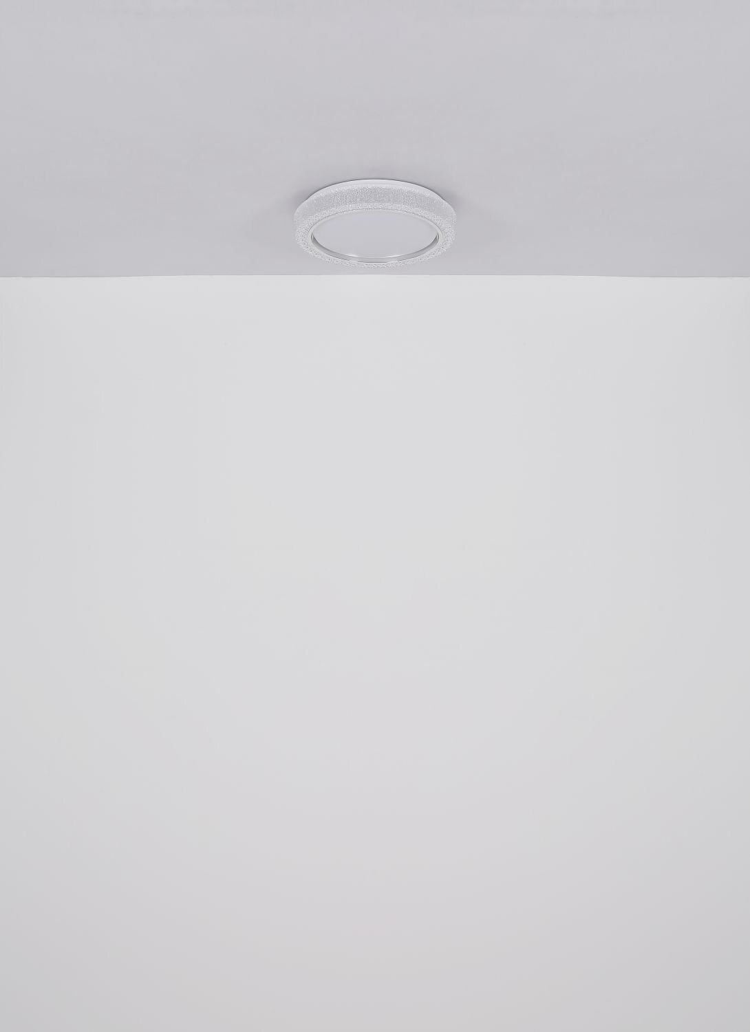 Na suficie zamontowana jest okrągła lampa sufitowa LED o nowoczesnym designie. Lampa ma jednolitą, jasną powierzchnię.