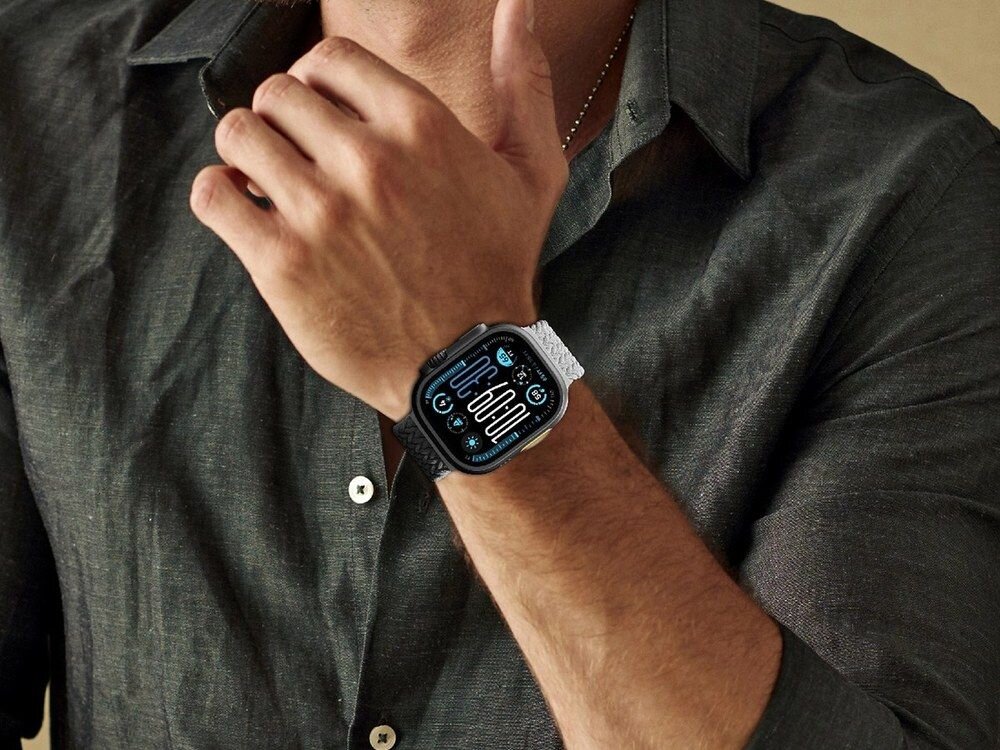 Apple Watch z szarym plecionym paskiem AmazingThing na nadgarstku mężczyzny w ciemnoszarej koszuli, ujęcie z boku.