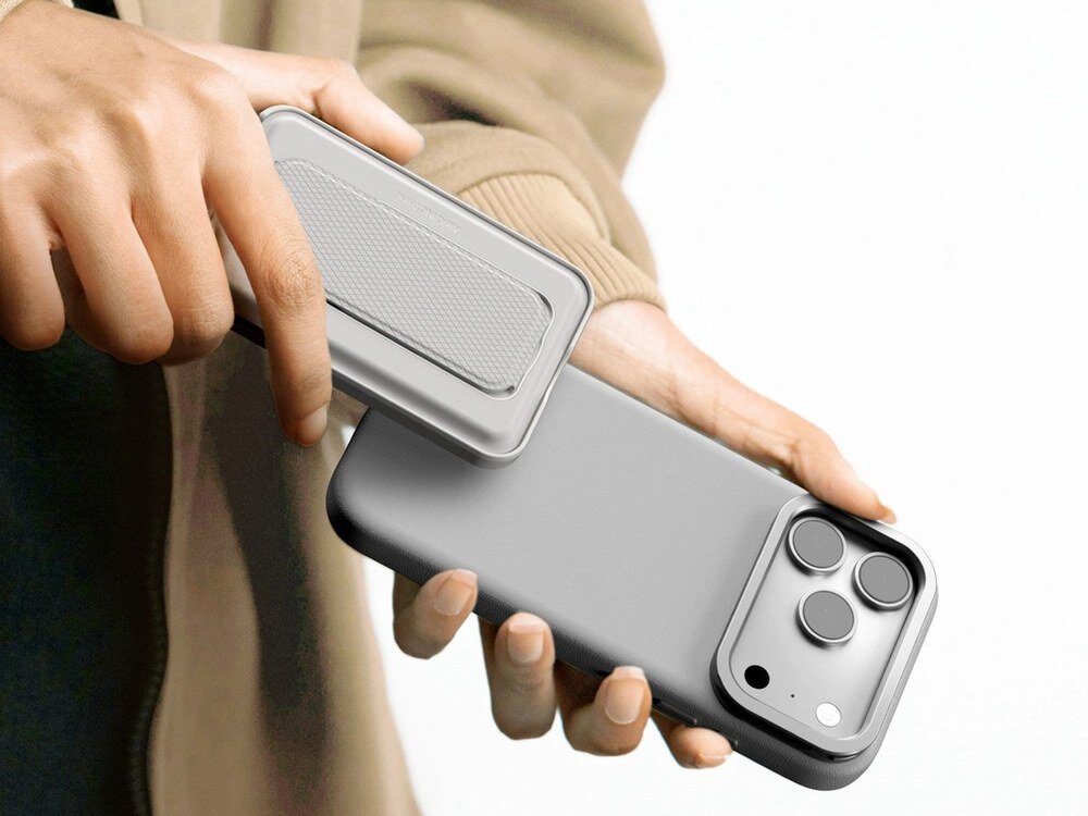 Szare etui AmazingThing Glamour na iPhone 17 Pro Max trzymane w dłoniach, widoczna wysuwana podstawka z modułem aparatu, ujęcie z tyłu.