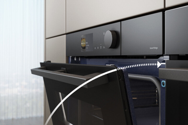 Obrazek pokazujący ciche domykanie piekarnika Samsung Steam Cook NV7B6785KA. Czarny piekarnik z otwartymi drzwiami, na panelu widoczny jest pokrętło i wyświetlacz z napisem \'SmartThings\'.