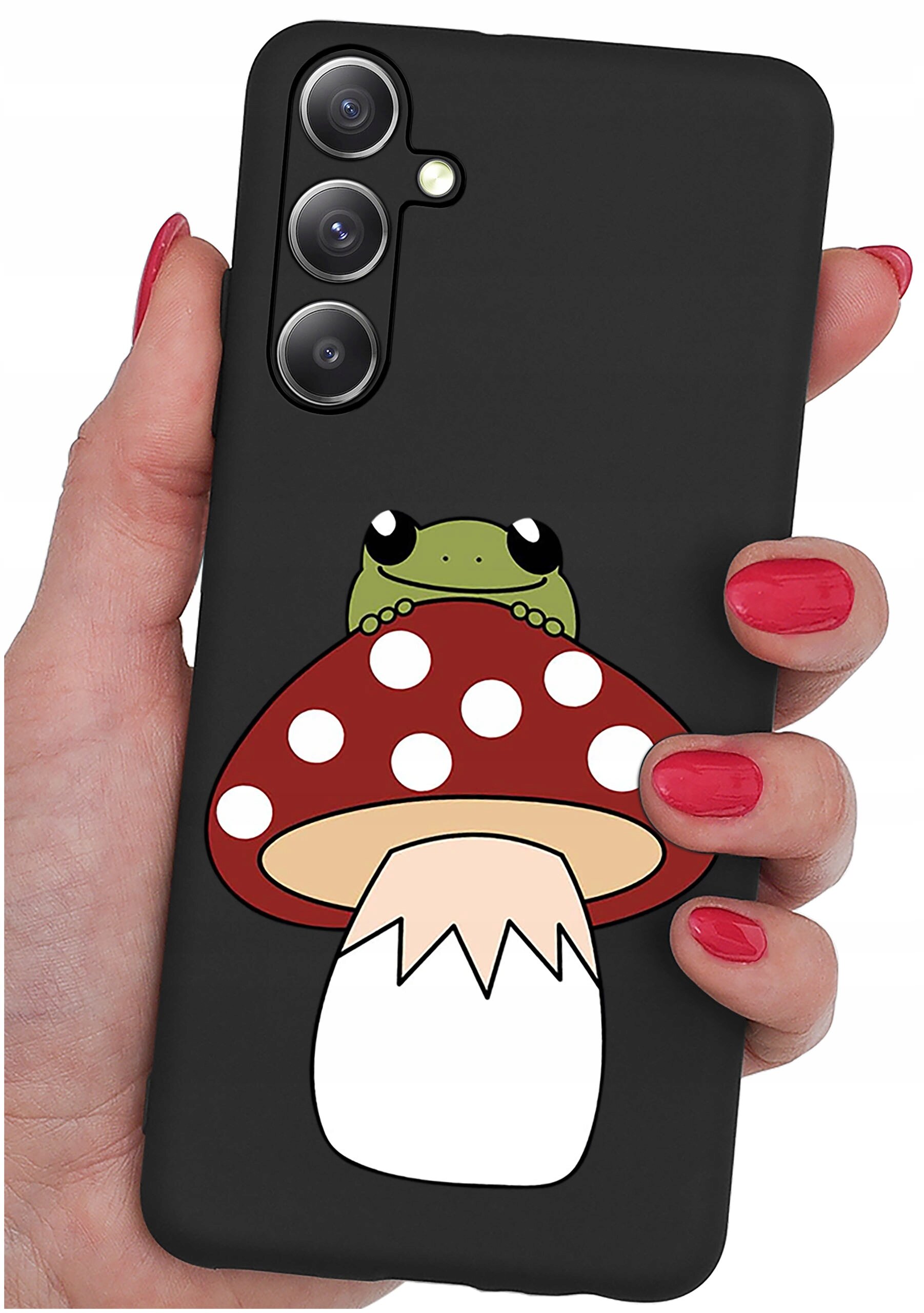 Czarne etui na telefon z grafiką przedstawiającą żabę siedzącą na czerwonym muchomorze z białymi kropkami. Etui trzymane jest w dłoni z pomalowanymi na czerwono paznokciami.