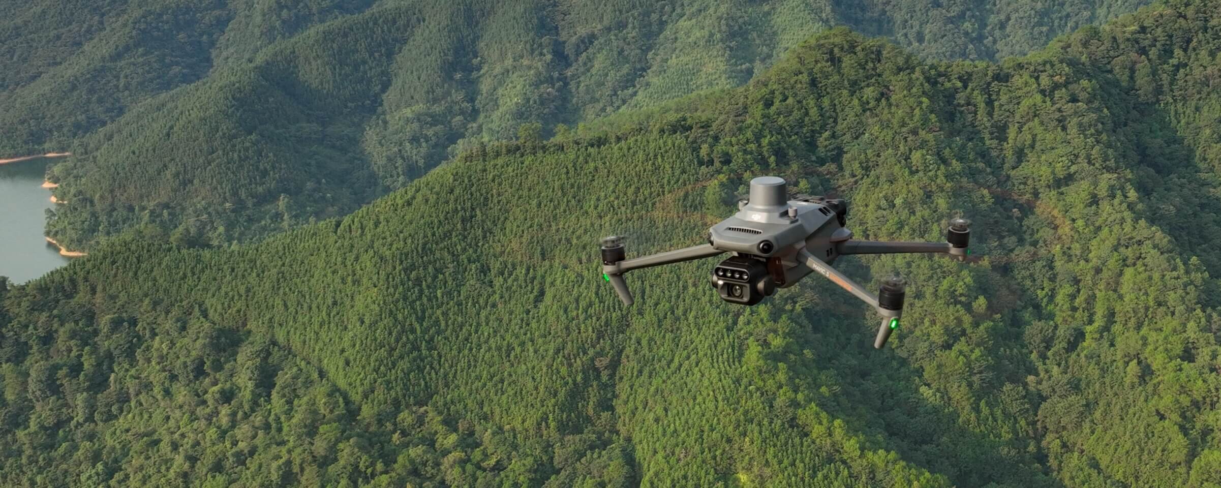 Dron unosi się nad zalesionym terenem, w tle widoczne są zielone wzgórza.