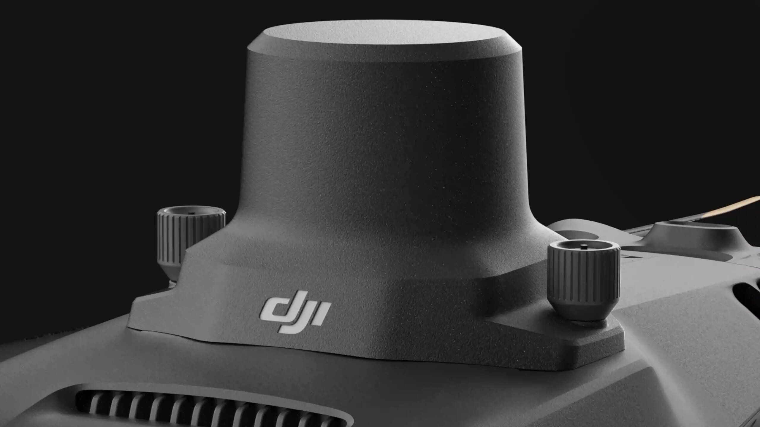 Zbliżenie na część drona z widocznym logo \'DJI\'. Element ma ciemny kolor i cylindryczny kształt.