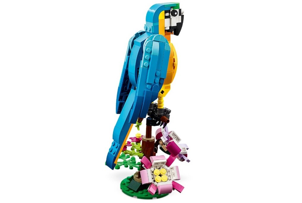 Model papugi z klocków LEGO w kolorach niebieskim, żółtym i czarnym, stojący na podstawce z zielonymi i różowymi elementami przypominającymi rośliny.