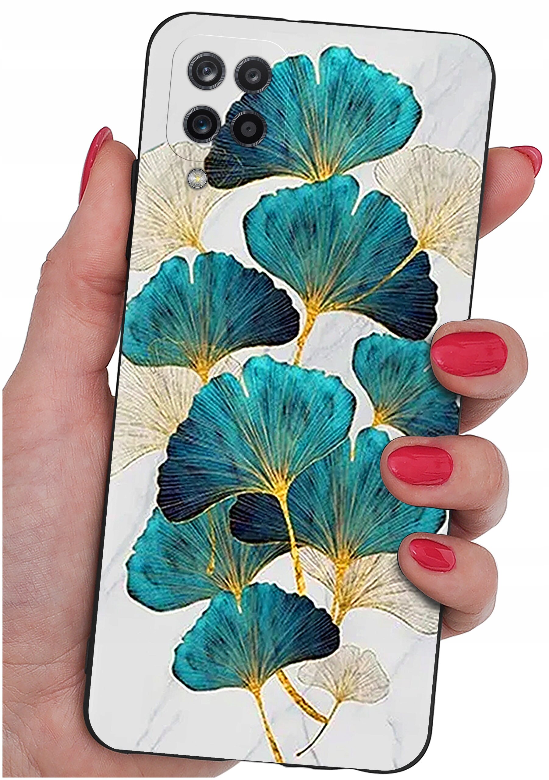 Etui na telefon z wzorem liści w odcieniach niebieskiego i złotego, trzymane w dłoni z pomalowanymi na czerwono paznokciami. Widoczne są cztery otwory na aparaty fotograficzne.