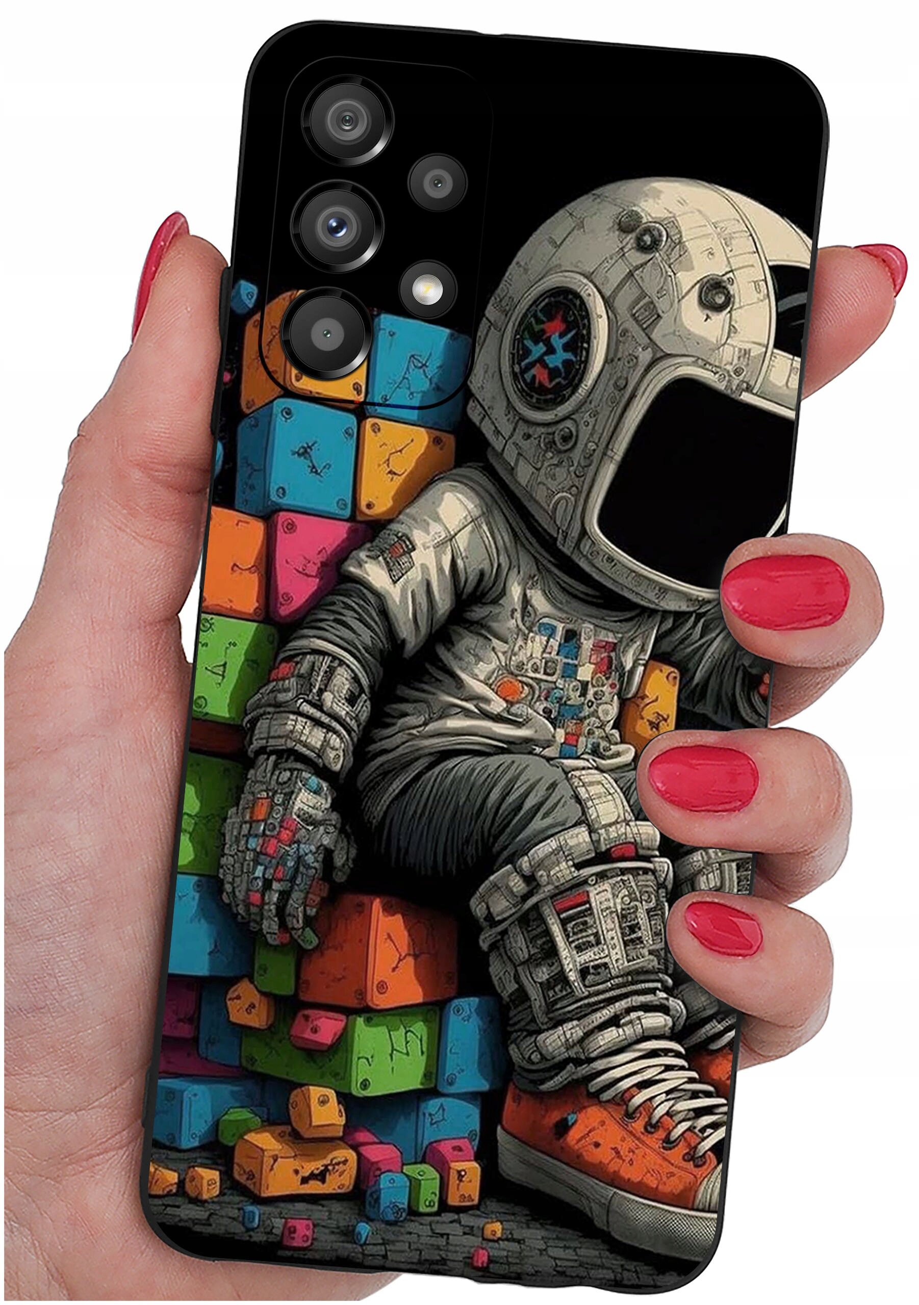 Etui na telefon z kolorowym nadrukiem przedstawiającym astronautę siedzącego na tle kolorowych klocków. Etui trzymane jest w dłoni z pomalowanymi na czerwono paznokciami.