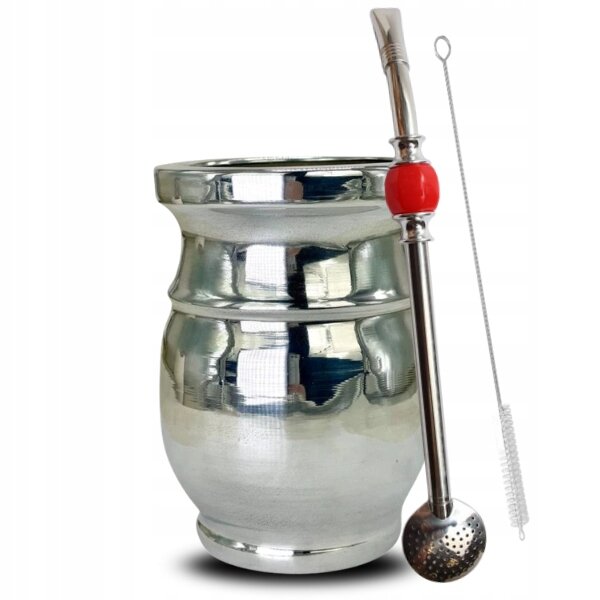 Na obrazie widoczny jest metalowy kubek o błyszczącej powierzchni oraz metalowa rurka z czerwonym elementem i sitkiem na końcu. Obok znajduje się szczoteczka do czyszczenia.