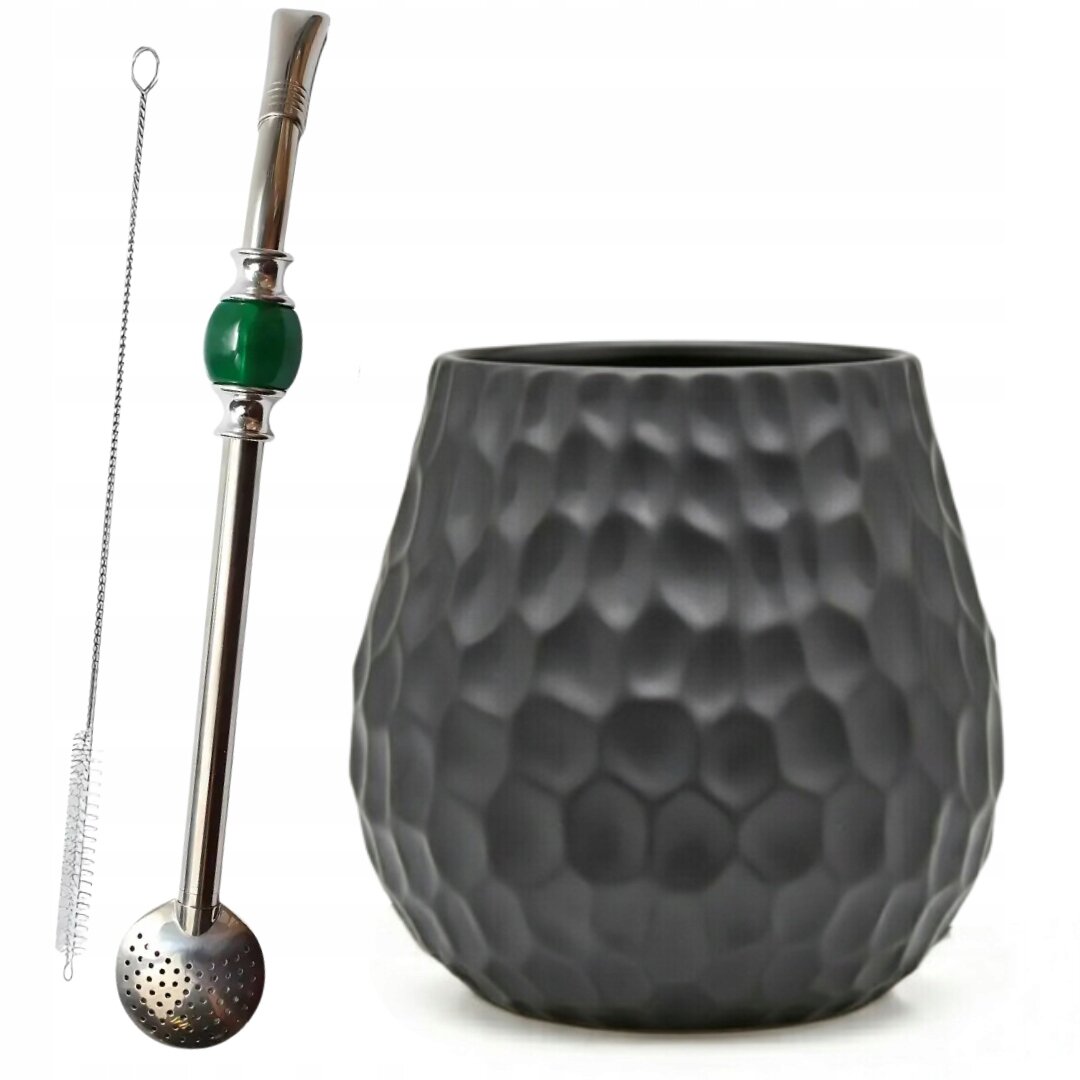 Na obrazie widoczny jest zestaw do yerba mate, składający się z czarnego, ceramicznego matero o fakturze przypominającej plaster miodu oraz metalowej bombilli z zielonym elementem i szczoteczką do czyszczenia.