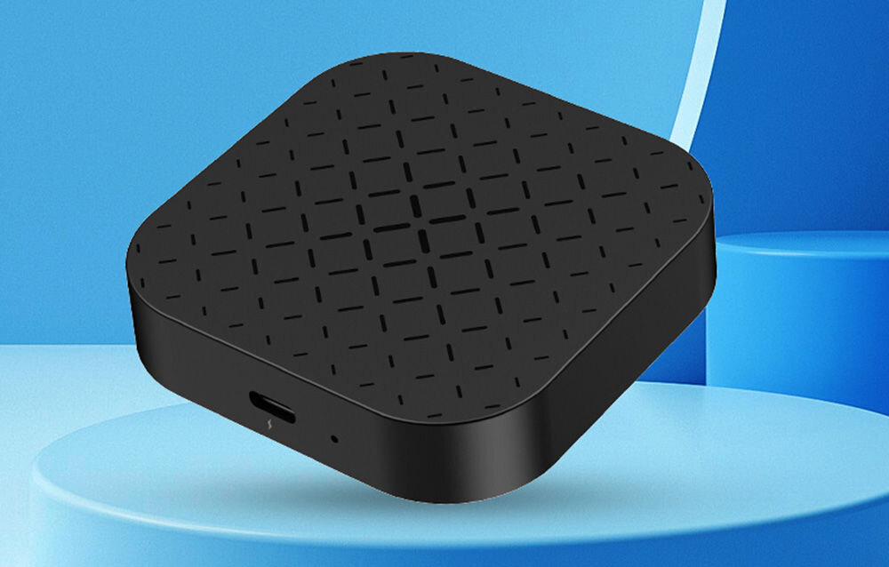 Czarny adapter o zaokrąglonych rogach z wzorem kratki na powierzchni, umieszczony na niebieskim tle. Widoczny jest port USB na boku urządzenia.