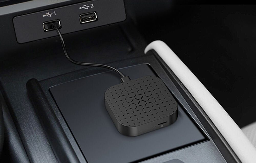 Na zdjęciu widać czarny adapter z wzorem na górnej powierzchni, podłączony kablem do portu USB oznaczonego numerem 1. Obok znajduje się drugi port USB oznaczony numerem 2.