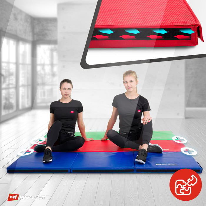 Dwie osoby siedzą na składanym, twardym materacu gimnastycznym w kolorach czerwonym, zielonym i niebieskim, z widocznym logo HOP SPORT. W prawym dolnym rogu znajduje się czerwony symbol z rzepami, a w lewym dolnym rogu logo HOP SPORT.