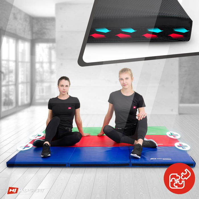 Dwie osoby siedzą na dużym, składanym materacu gimnastycznym w kolorach niebieskim, czerwonym i zielonym. W prawym dolnym rogu widoczne jest logo HOP SPORT oraz symbol złożenia materaca.