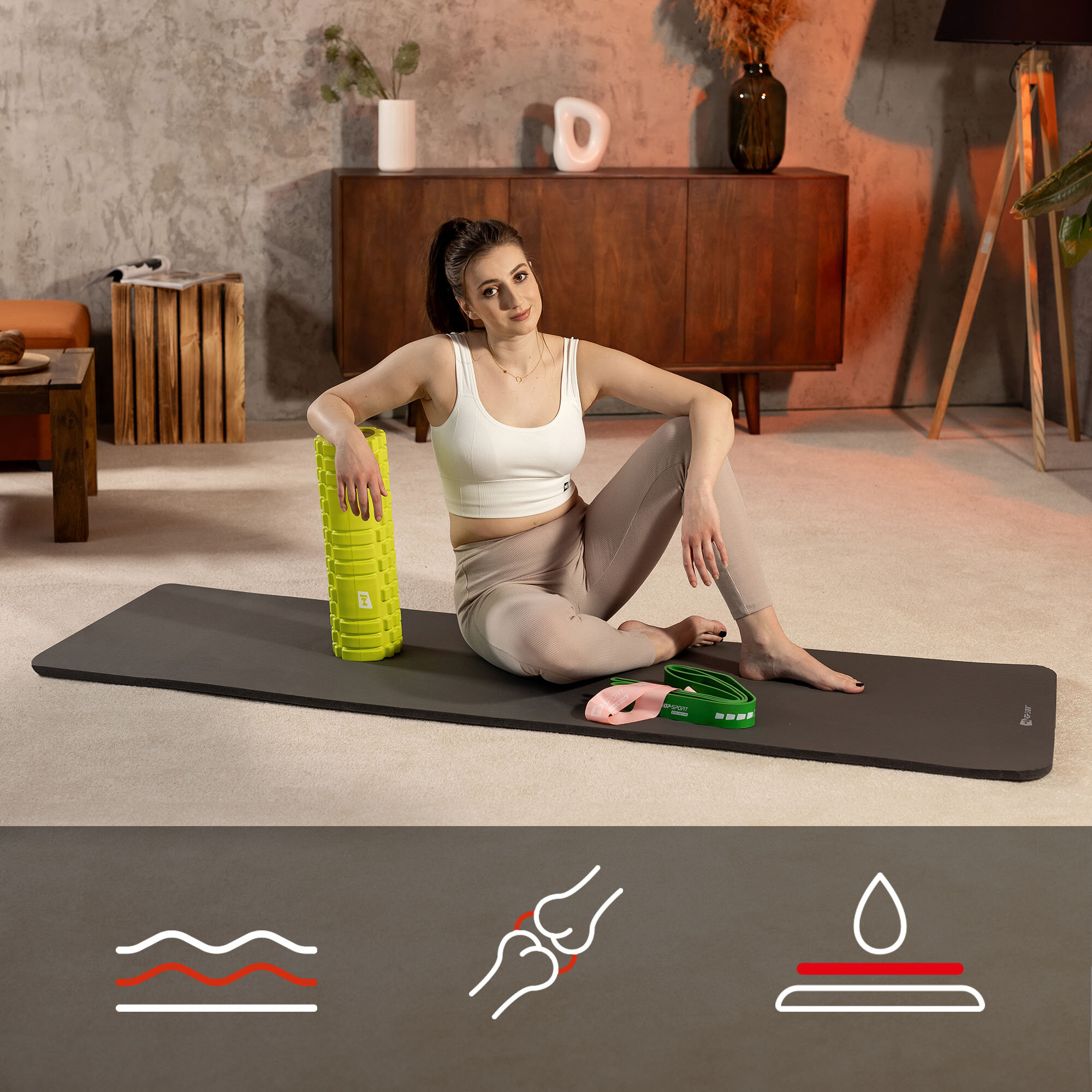 Osoba siedzi na szarej macie fitness NBR o wymiarach 190x60 cm, trzymając zielony wałek do ćwiczeń. W tle znajduje się drewniana komoda i dekoracje, a na dole obrazu widoczne są ikony przedstawiające fale, stawy i kroplę wody.