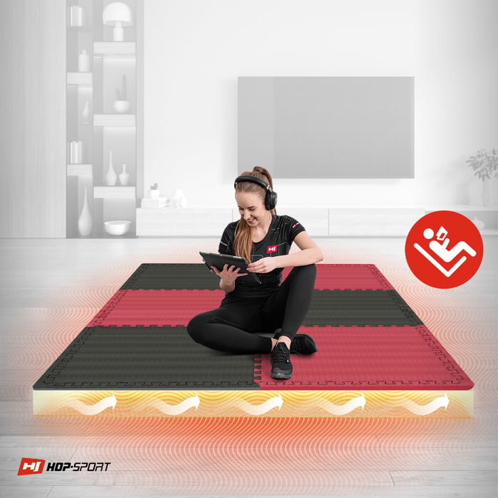 Osoba siedzi na macie puzzle EVA w kolorach czarnym i czerwonym, trzymając tablet. W rogu widoczne jest logo HOP-SPORT oraz ikona z symbolem osoby ćwiczącej.