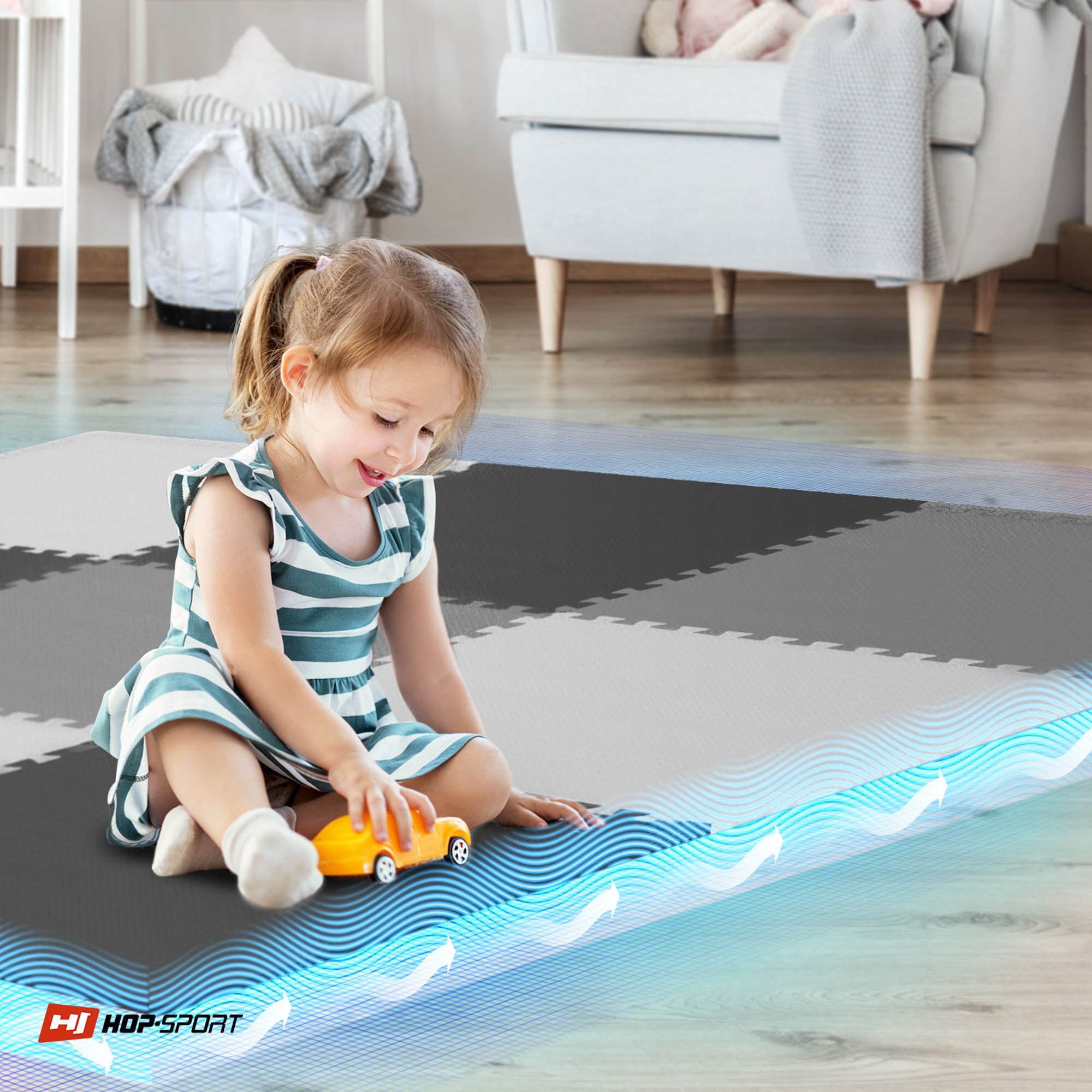 Dziecko bawi się na macie puzzle w kolorach czarnym, białym i szarym, trzymając pomarańczowy samochodzik. W rogu widoczne jest logo \'HOP-SPORT\'.
