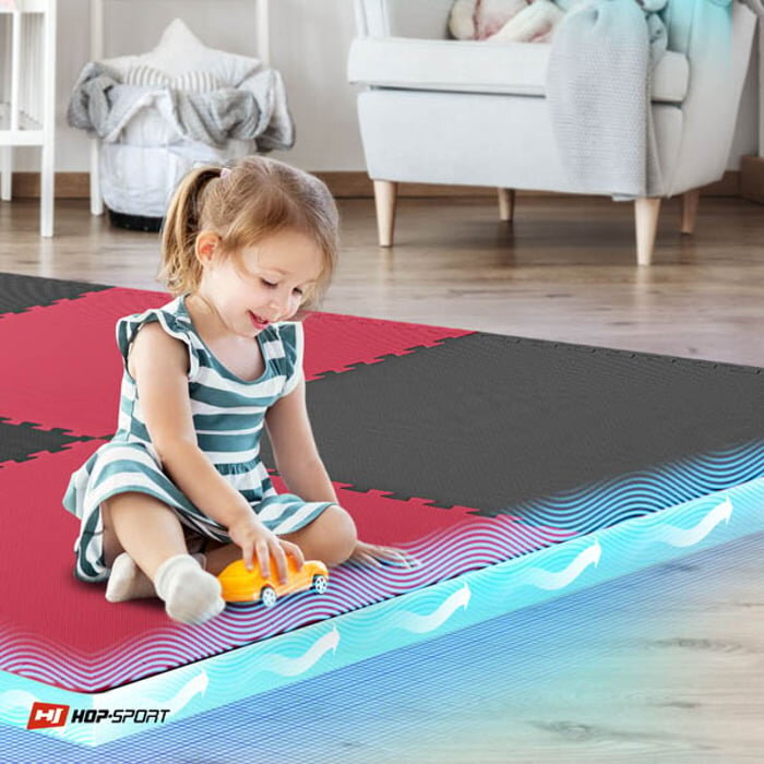 Dziewczynka bawi się na macie puzzle w kolorach czarnym i czerwonym. W rogu widoczne jest logo \'HOP-SPORT\'.