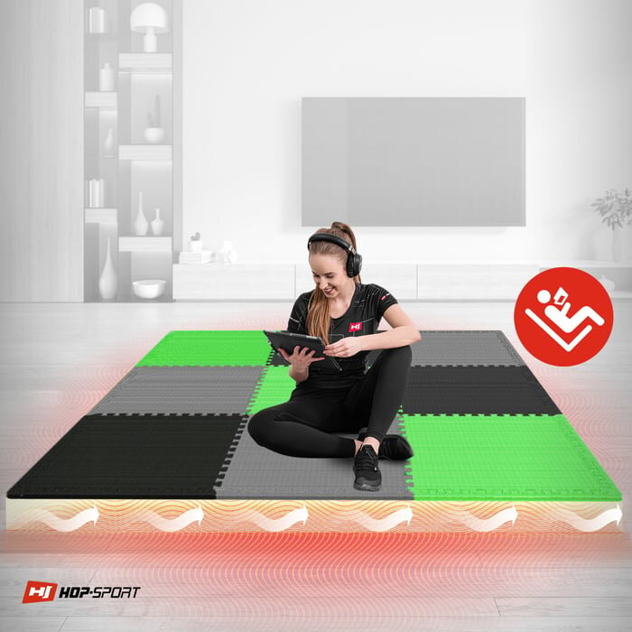Na obrazie widać matę puzzle w kolorach czarnym, szarym i zielonym, na której siedzi osoba z tabletem i słuchawkami. W lewym dolnym rogu znajduje się logo \'HOP-SPORT\'.
