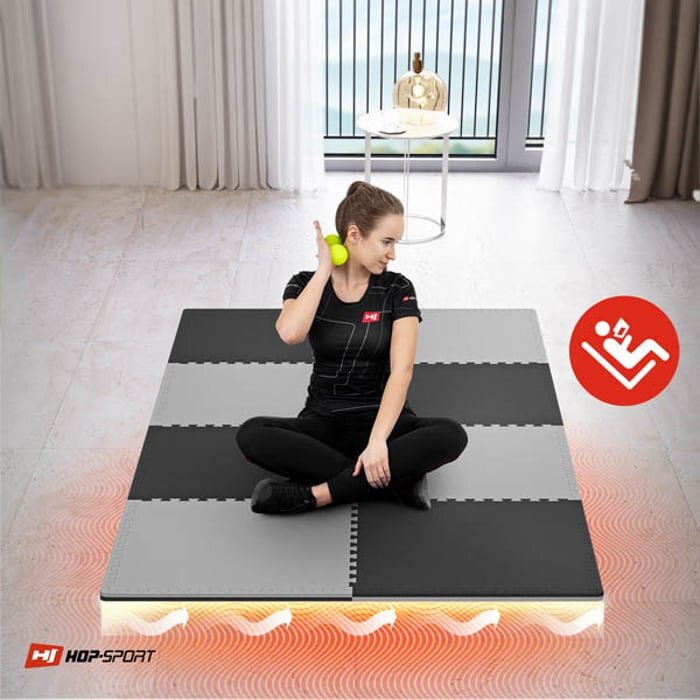 Osoba siedzi na czarno-szarej macie puzzle EVA, trzymając piłkę. W rogu widoczne jest logo HOP-SPORT oraz czerwony symbol z postacią ćwiczącą.