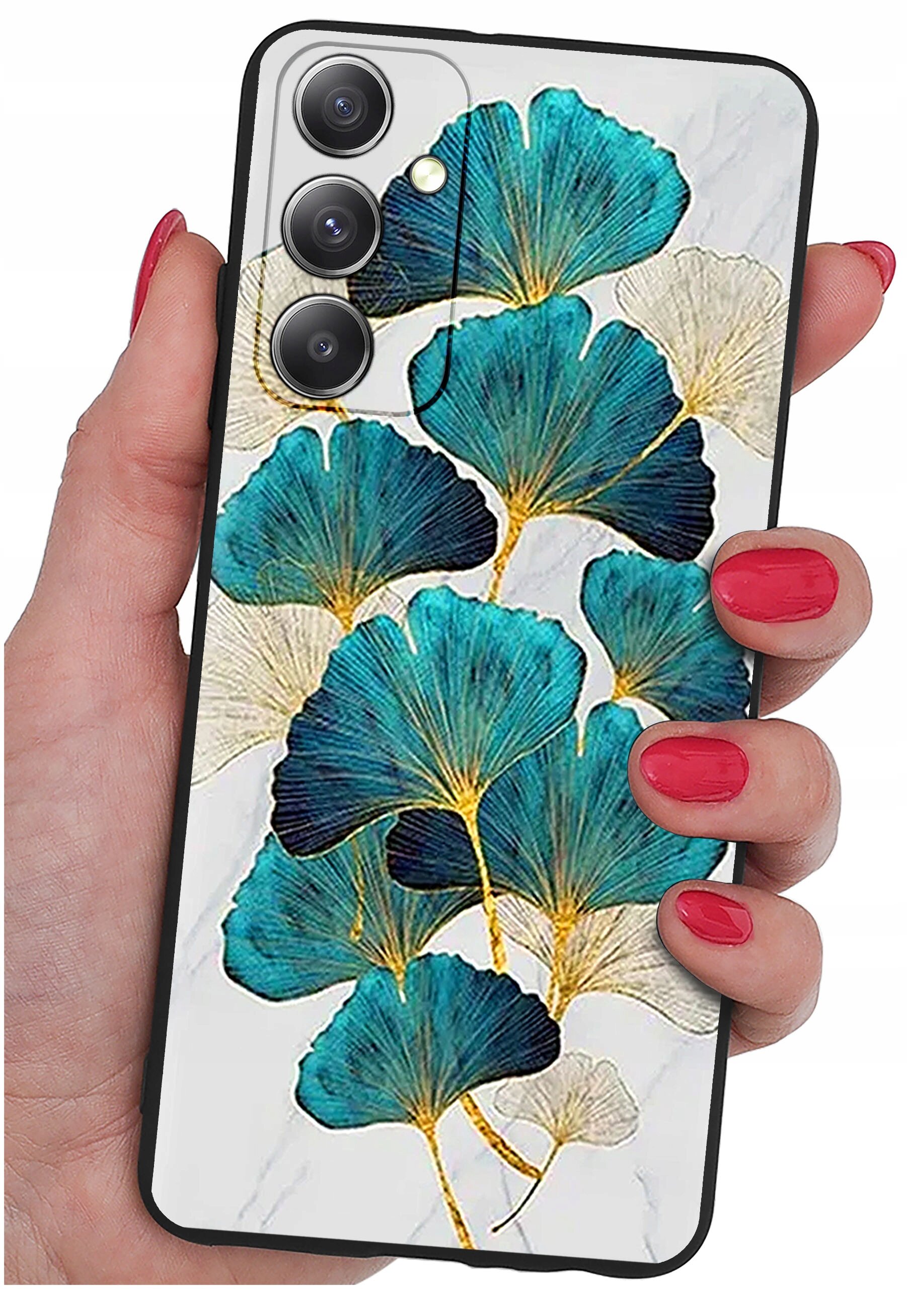 Etui na telefon z wzorem liści w odcieniach niebieskiego i złotego, trzymane w dłoni z pomalowanymi na czerwono paznokciami. Etui posiada trzy otwory na aparaty fotograficzne.