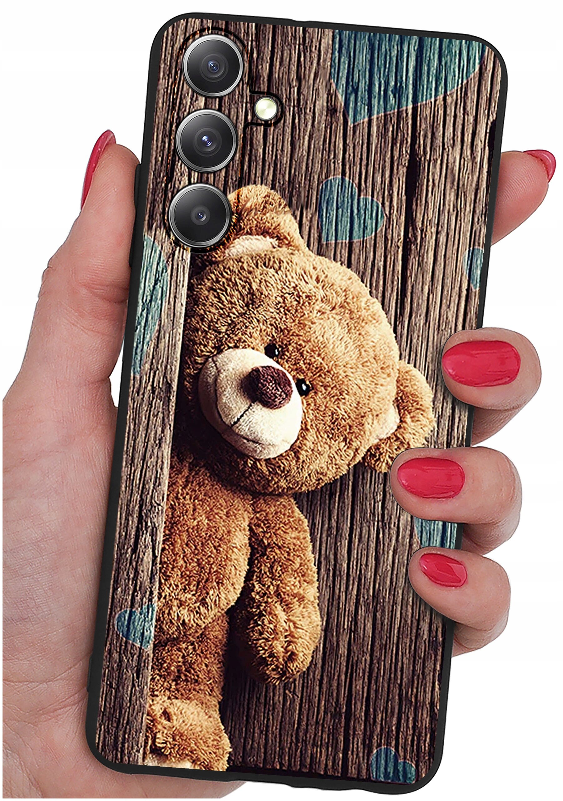 Etui na telefon z nadrukiem misia na tle drewnianych desek z niebieskimi sercami, trzymane w dłoni z pomalowanymi na czerwono paznokciami.