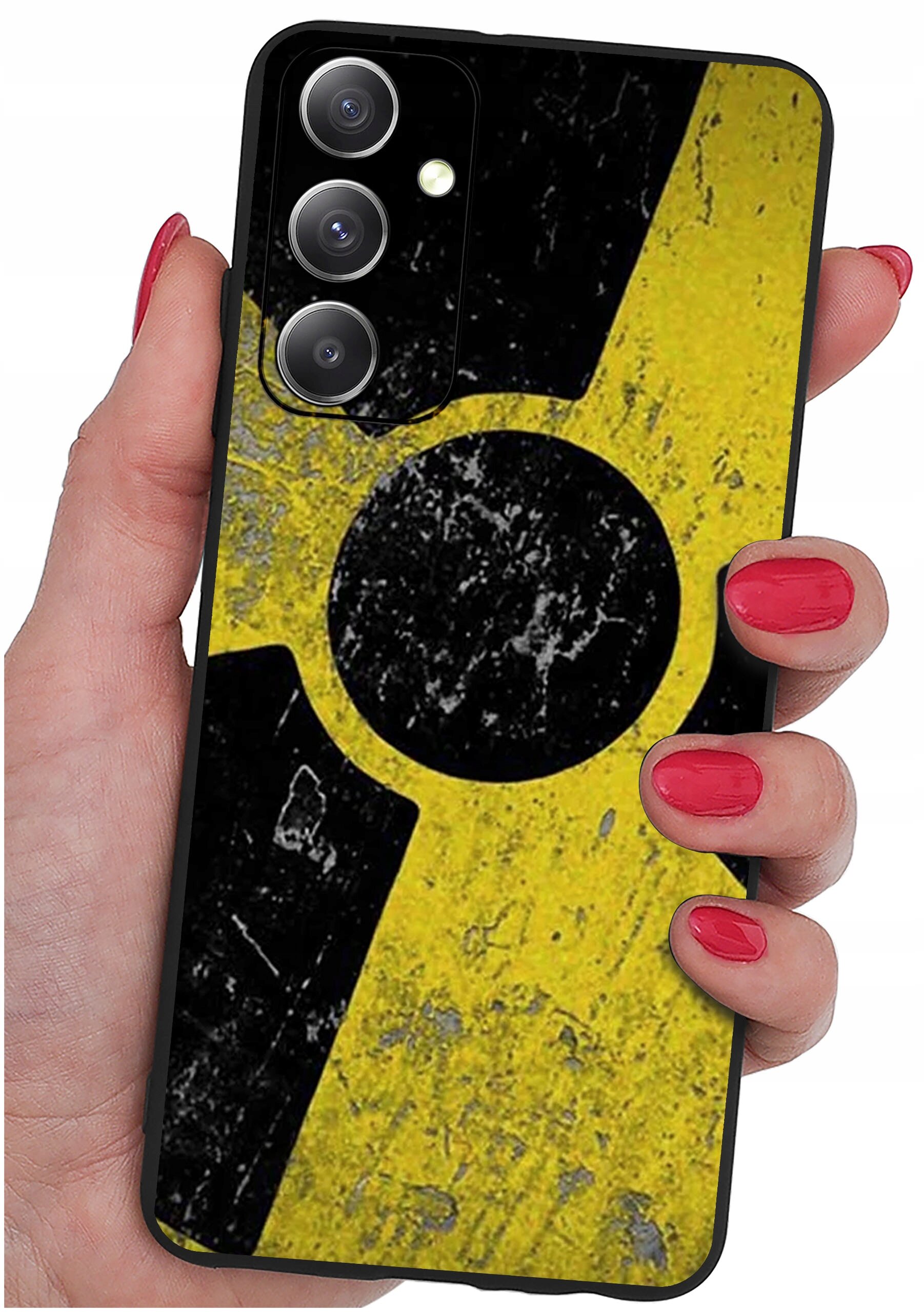 Etui na telefon z żółto-czarnym wzorem przypominającym symbol promieniowania, trzymane w dłoni z pomalowanymi na czerwono paznokciami. Widoczne są trzy obiektywy aparatu i lampa błyskowa.