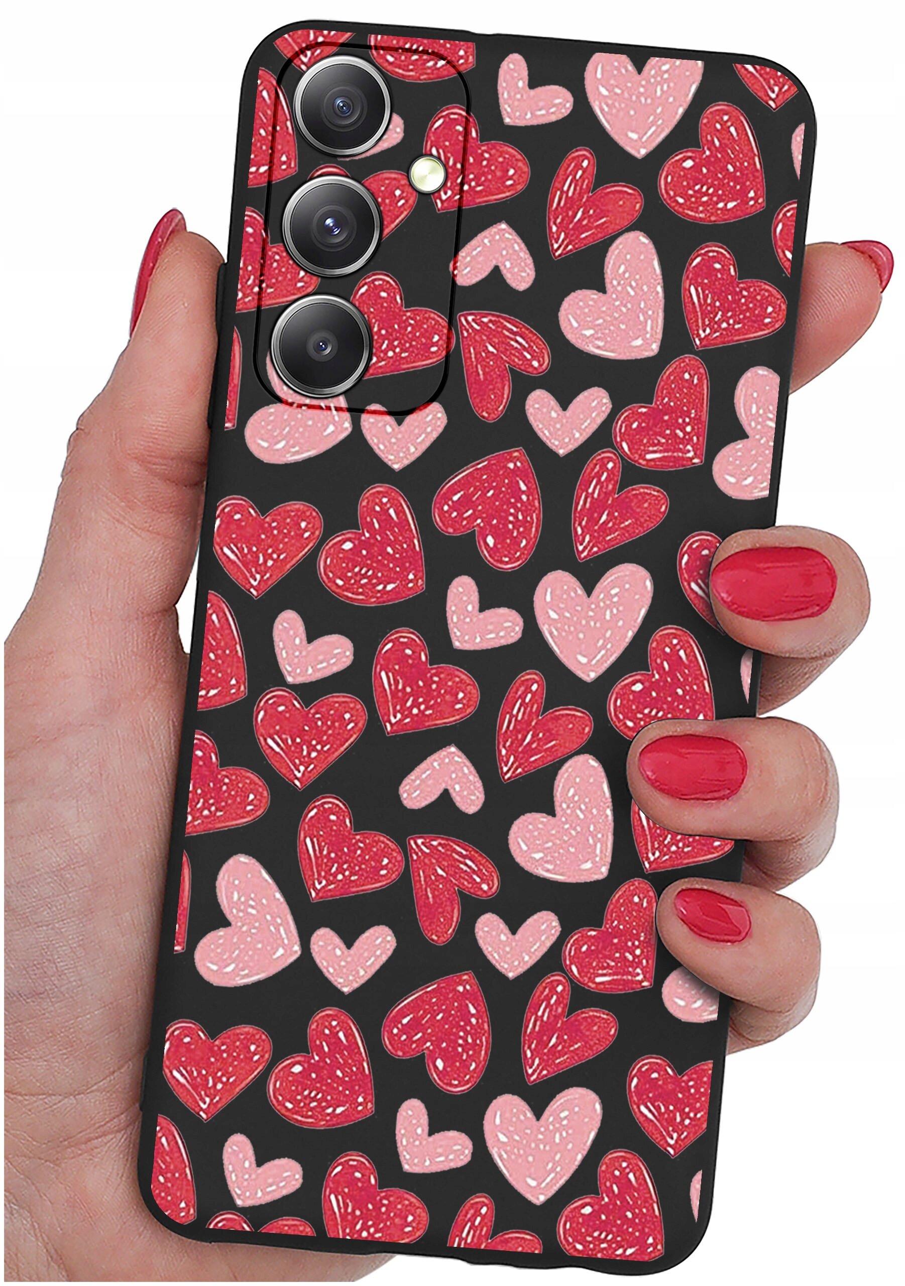 Etui na telefon z wzorem czerwonych i różowych serc na czarnym tle, trzymane w dłoni z pomalowanymi na czerwono paznokciami. Widoczne są trzy obiektywy aparatu i lampa błyskowa.