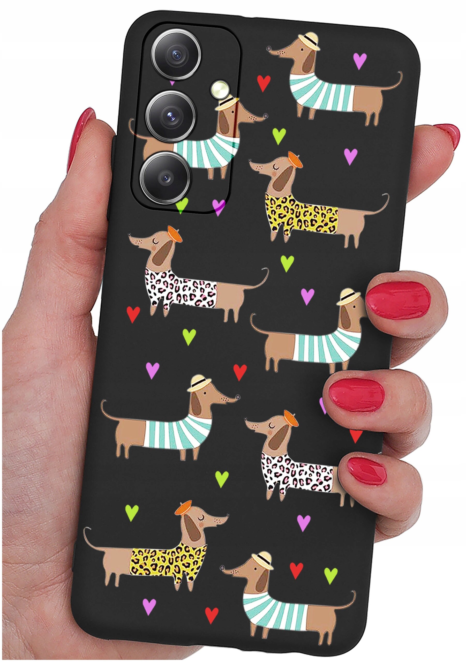 Czarne etui na telefon z wzorem przedstawiającym psy w kolorowych ubrankach i kapeluszach, otoczone kolorowymi serduszkami. Etui trzymane jest w dłoni z pomalowanymi na czerwono paznokciami.