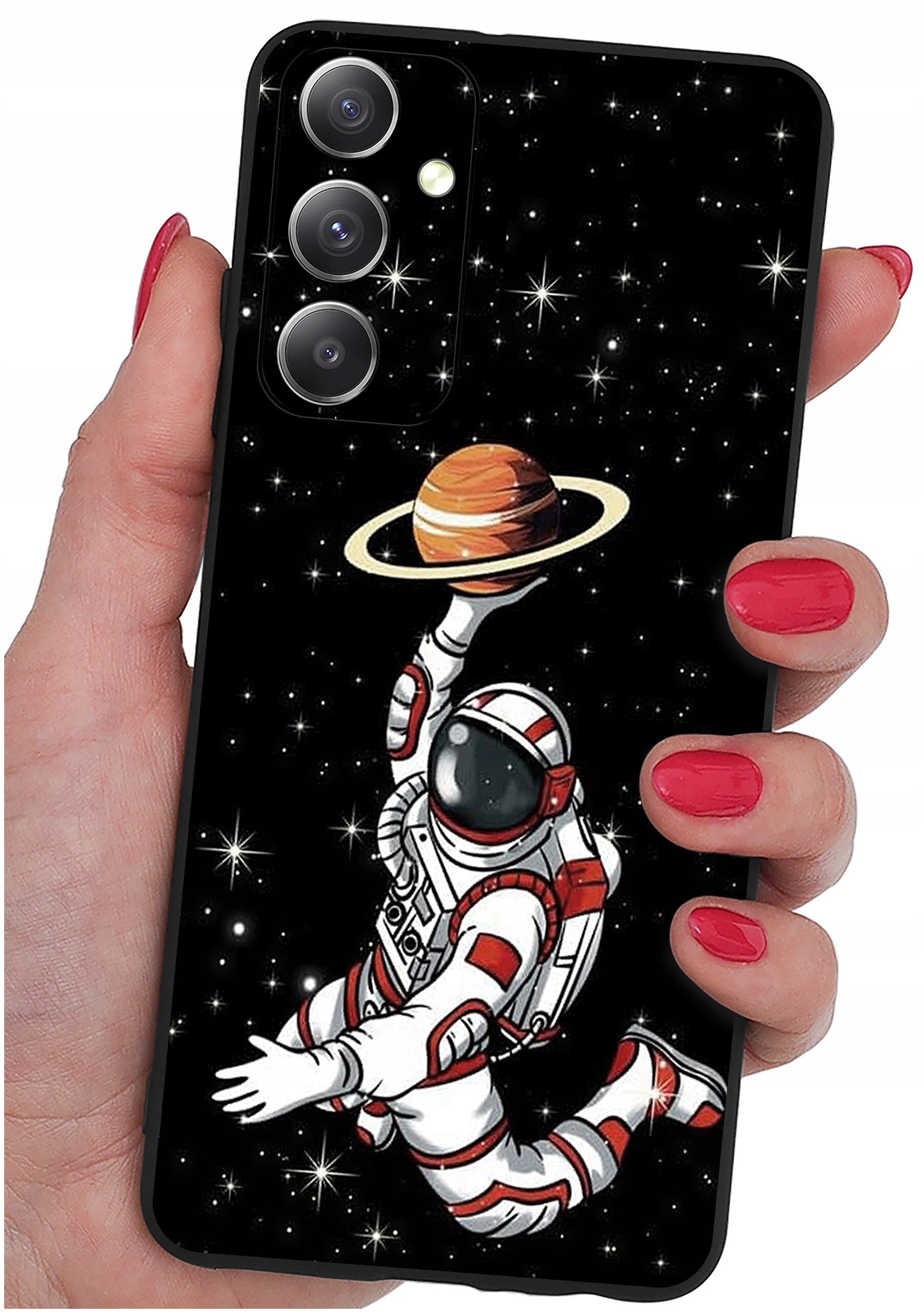 Etui na telefon z grafiką przedstawiającą astronautę unoszącego planetę z pierścieniami na tle gwiazd. Etui trzymane jest w dłoni z pomalowanymi na czerwono paznokciami.