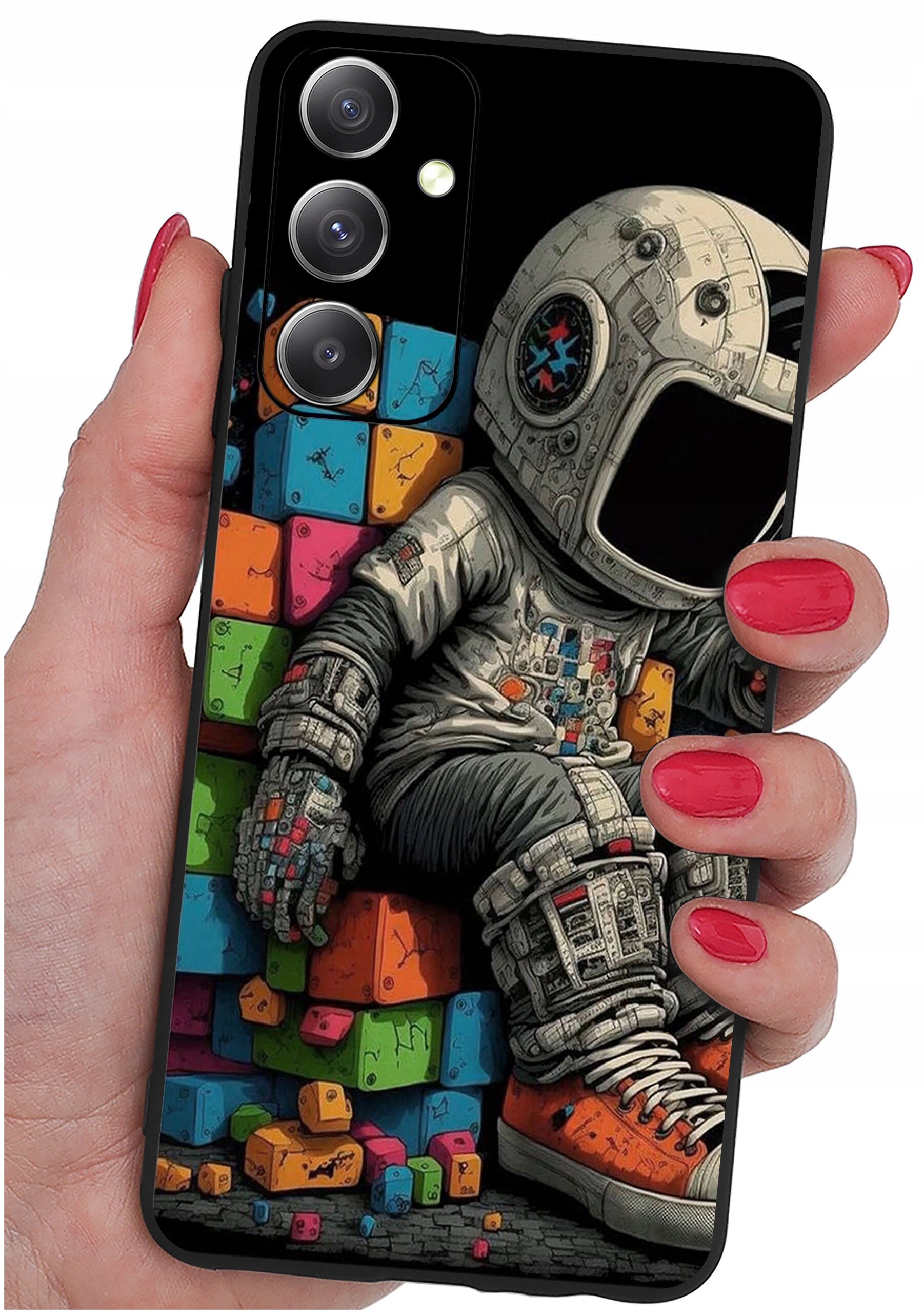 Etui na telefon z kolorowym nadrukiem przedstawiającym astronautę siedzącego na tle kolorowych klocków. Etui trzymane jest w dłoni z pomalowanymi na czerwono paznokciami.