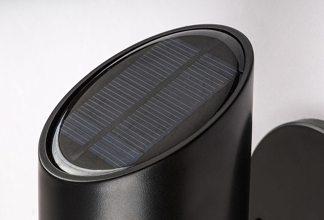 Obraz przedstawia czarny, cylindryczny kinkiet zewnętrzny z panelem solarnym na górze. Panel ma kształt owalny i jest umieszczony na gładkiej powierzchni urządzenia.