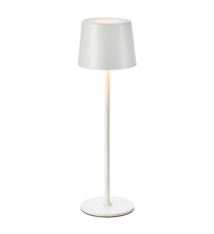 Biała lampa stołowa z prostym, cylindrycznym kloszem i smukłą podstawą. Lampa emituje delikatne światło z górnej części klosza.