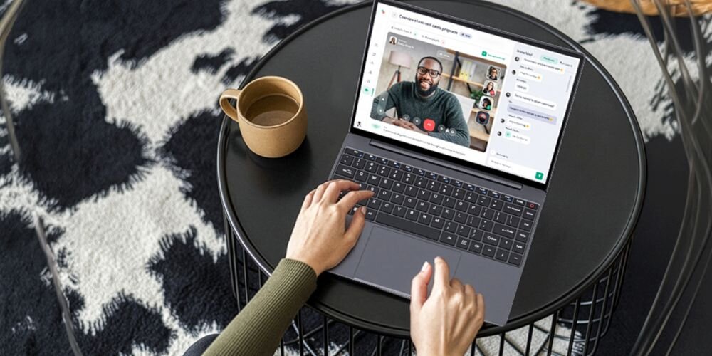 Osoba korzysta z laptopa podczas wideorozmowy przy okrągłym stoliku z kubkiem kawy