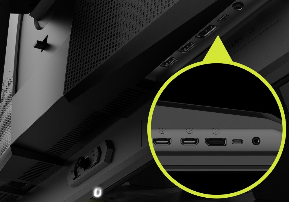 Zdjęcie przedstawia tylną część monitora z widocznymi portami: dwa HDMI, DisplayPort, USB-C i gniazdo audio. Obraz jest w odcieniach szarości z żółtym okręgiem powiększającym widok portów.
