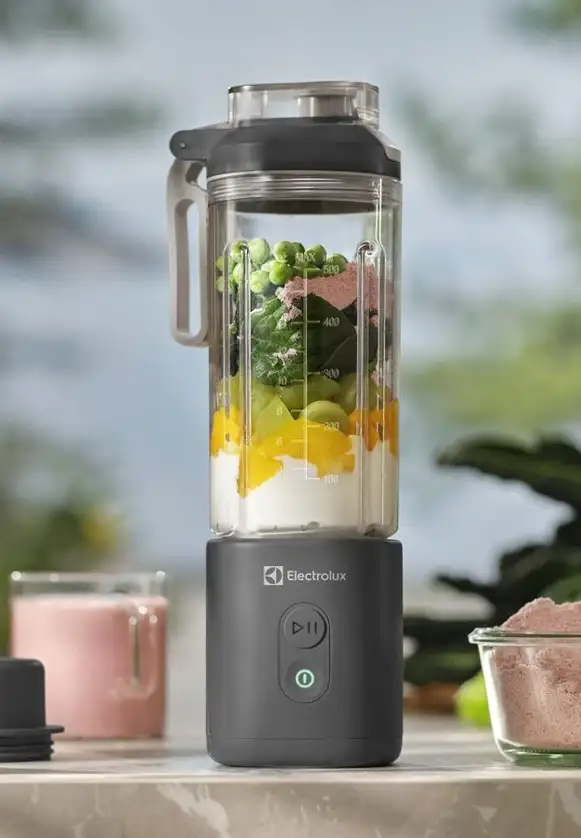 Blender personalny z logo Electrolux, wypełniony składnikami do smoothie, stoi na blacie. Obok znajdują się szklanka z różowym napojem i miseczka z proszkiem.