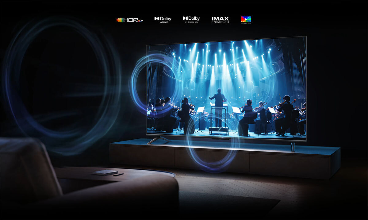 Telewizor wyświetla obraz orkiestry na scenie w jasnym, niebieskim świetle. Na górze ekranu widoczne są loga: HDR, Dolby Atmos, Dolby Vision IQ, IMAX Enhanced.