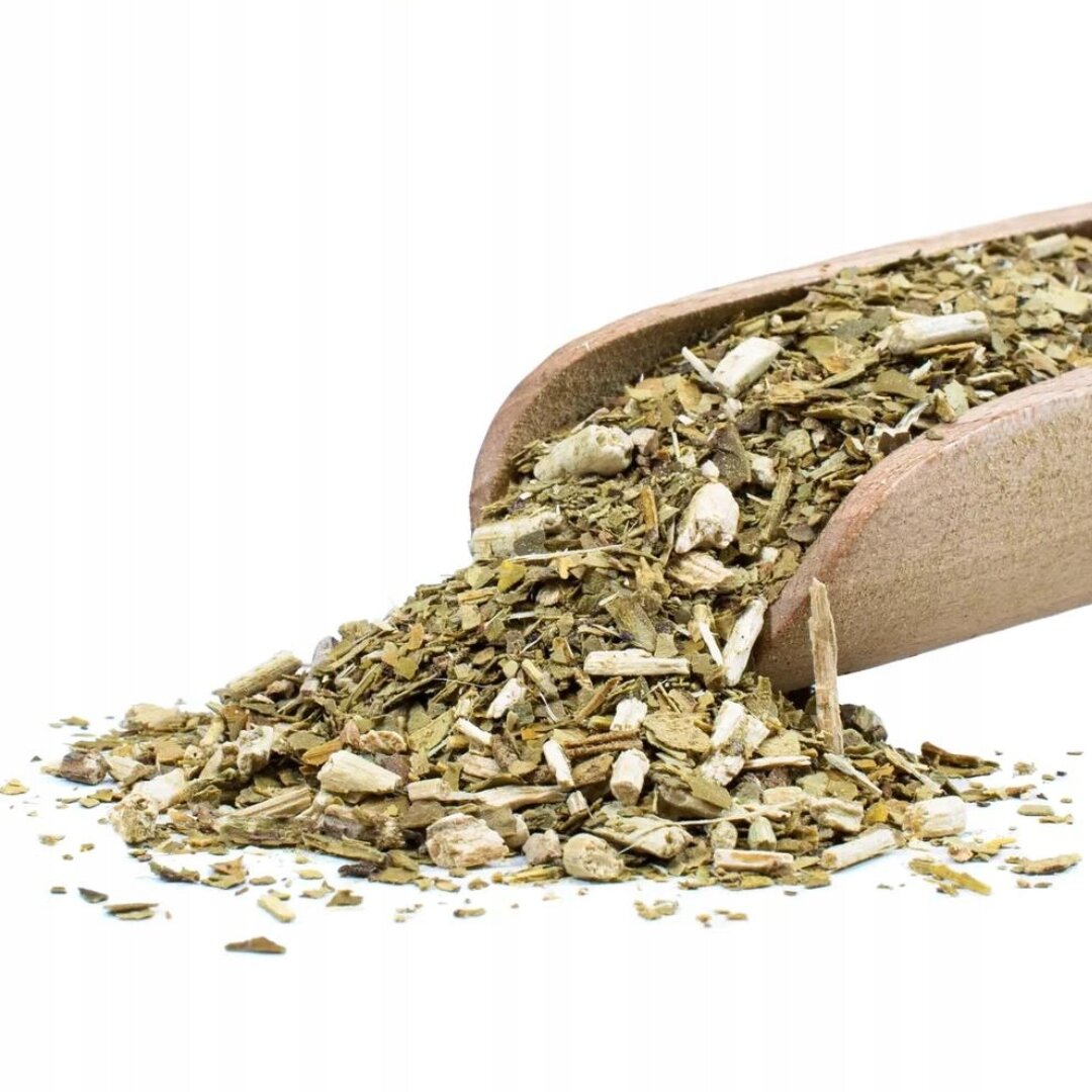 Na obrazie widoczna jest drewniana łopatka, z której wysypuje się susz yerba mate. Susz składa się z drobnych liści i gałązek w odcieniach zieleni i brązu.