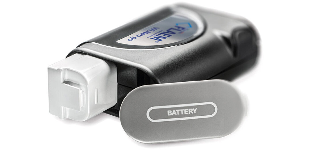 Na zdjęciu widoczny jest inhalator nebulizator pneumatyczny z napisem \'FLAEM Wi.Neb Go\'. Obok urządzenia znajduje się element z napisem \'BATTERY\'.