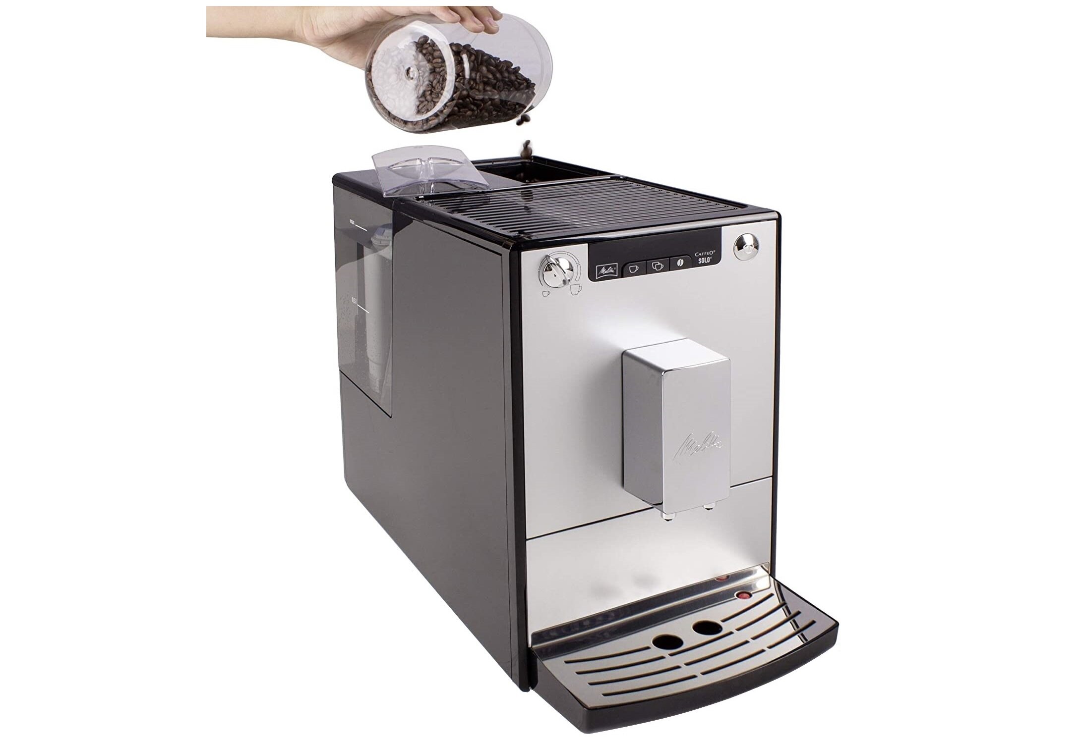 Ekspres do kawy w kolorze czarno-srebrnym z widocznym logo \'Melitta\' na przednim panelu. Ręka wsypuje ziarna kawy do pojemnika na górze urządzenia.