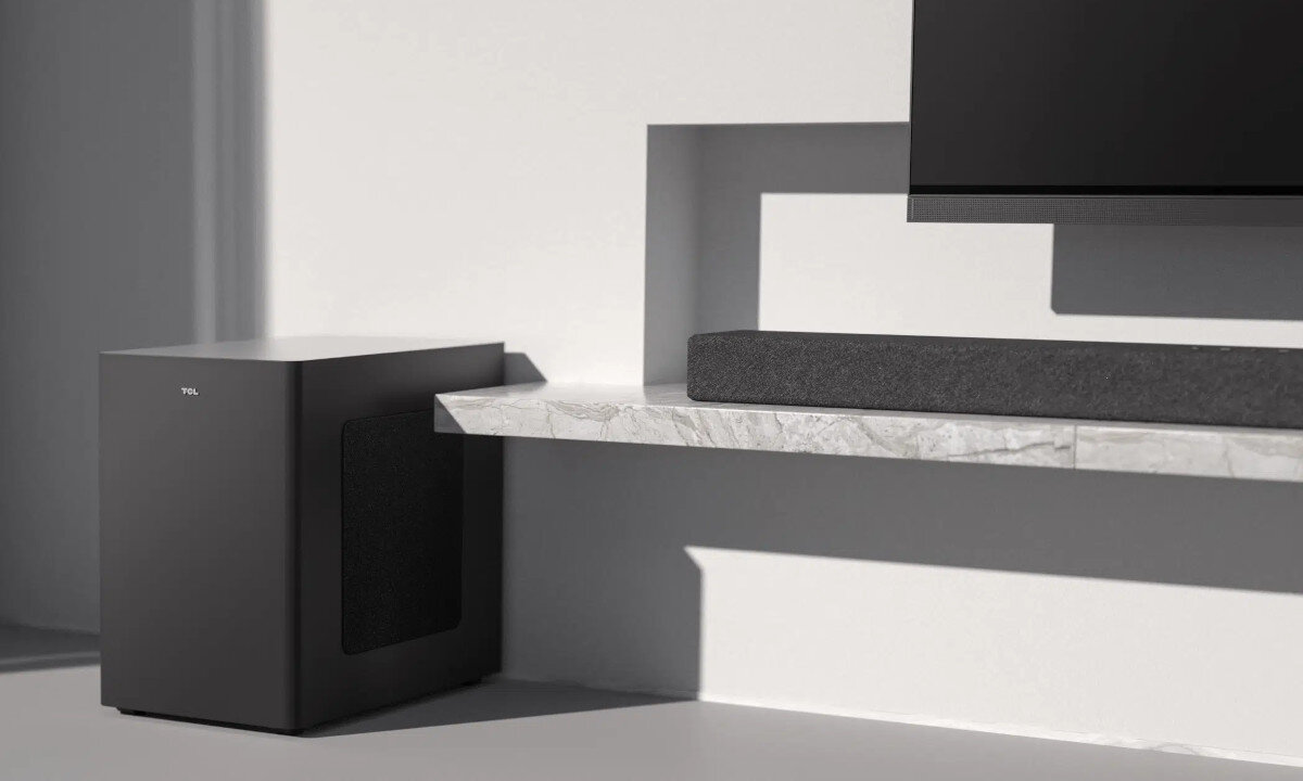 Na obrazie widoczny jest soundbar i subwoofer w minimalistycznym wnętrzu. Na subwooferze znajduje się logo \'TCL\'.