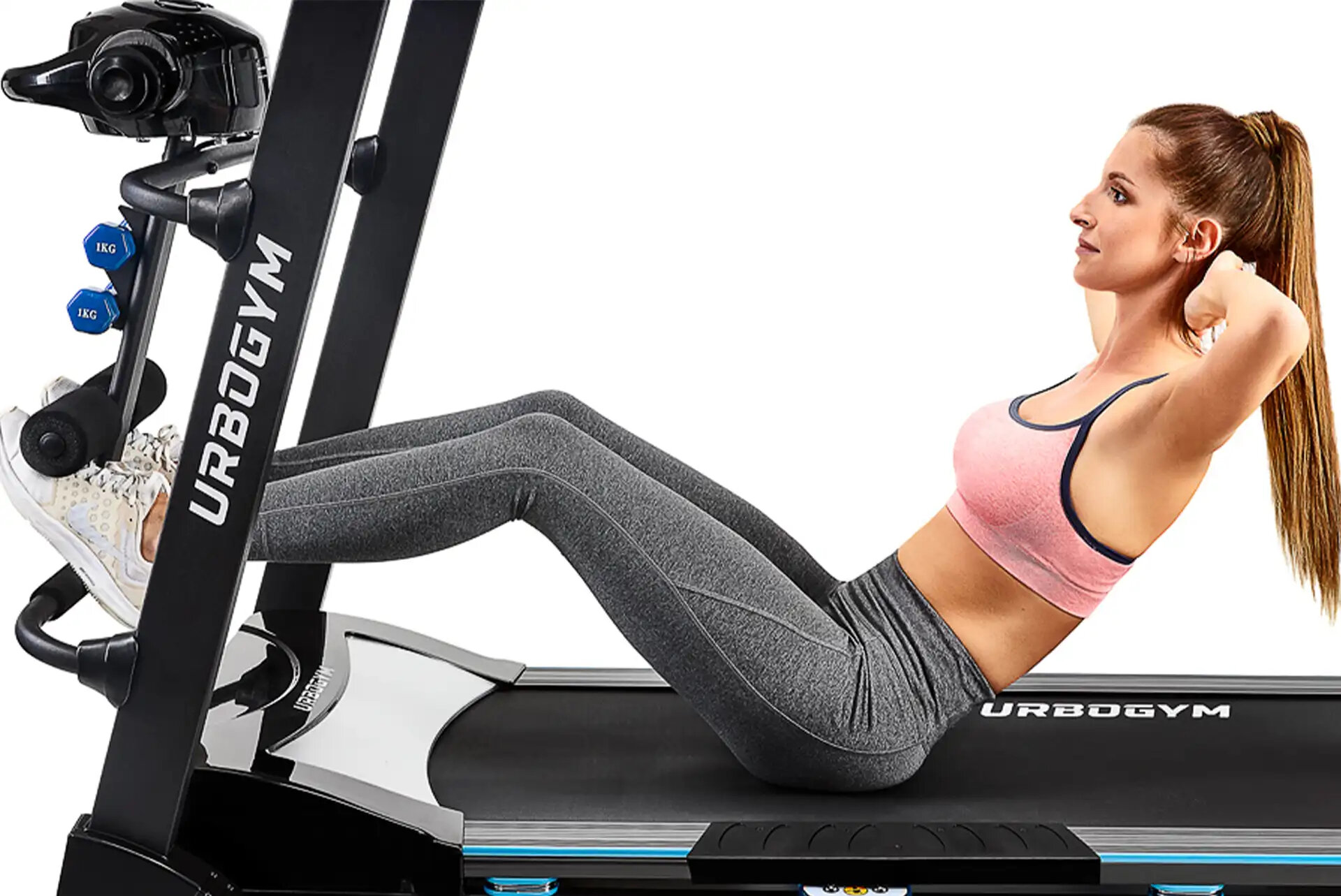 Osoba ćwiczy na bieżni elektrycznej, wykonując brzuszki. Na bieżni widoczne jest logo \'URBOGYM\'.