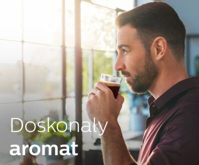 Mężczyzna trzymający filiżankę z napojem, stojący przy oknie. Na obrazie widoczny jest tekst: \'Doskonały aromat\'.