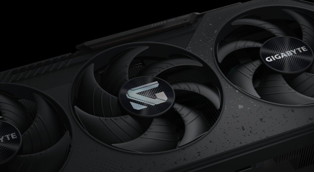 Karta graficzna GIGABYTE Radeon RX 9070 GRE Gaming OC Zbliżenie na obudowę karty graficznej i jej dwa wentylatory, z widocznym logo w centralnej części oraz drobno teksturowaną powierzchnią