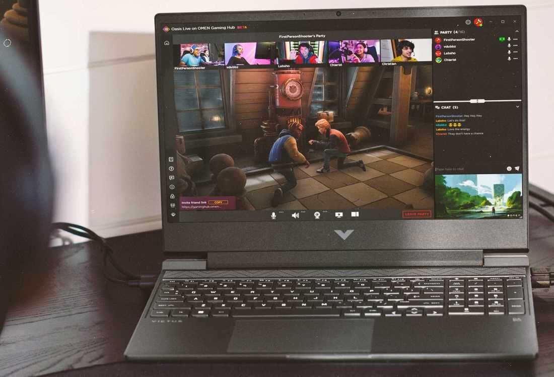 Laptop z otwartym ekranem, na którym wyświetlana jest gra wideo oraz okna czatu i transmisji na żywo. Na obudowie widoczne jest logo w kształcie litery V.
