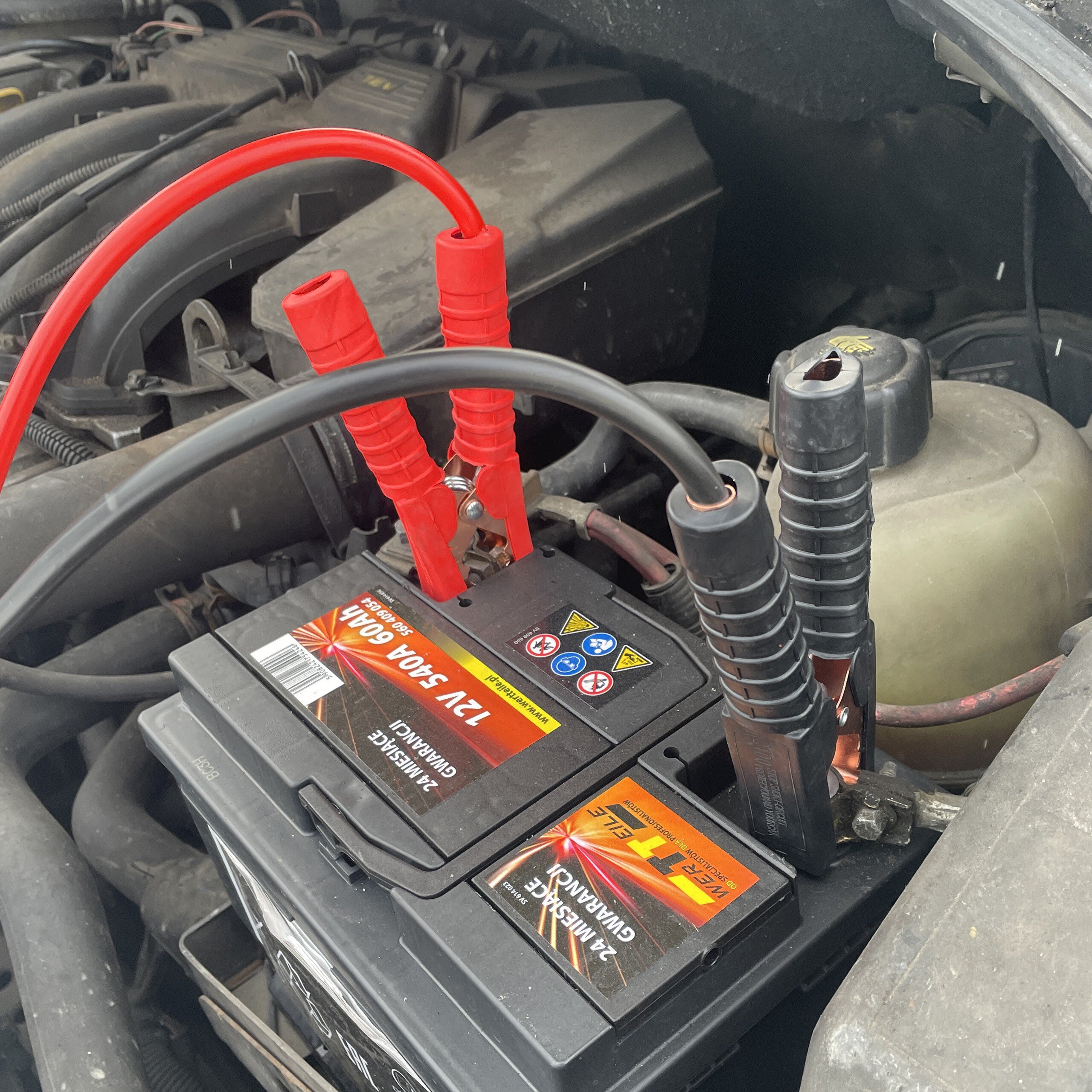 Na zdjęciu widać akumulator samochodowy z podłączonymi kablami rozruchowymi. Na akumulatorze widoczny jest tekst: \'12V 540A 60Ah\'.