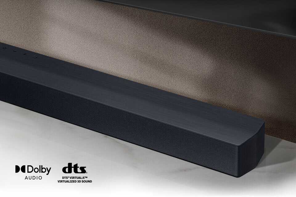Czarny soundbar umieszczony na jasnej powierzchni, z widocznymi logotypami \'Dolby Audio\' i \'DTS Virtual:X Virtualized 3D Sound\'.