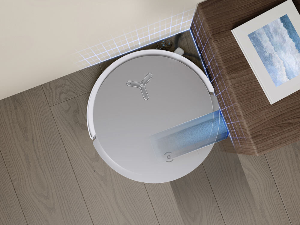 Na podłodze znajduje się biały robot sprzątający o okrągłym kształcie, obok drewnianego mebla z obrazem. Robot emituje niebieską siatkę świetlną na ścianę i mebel.