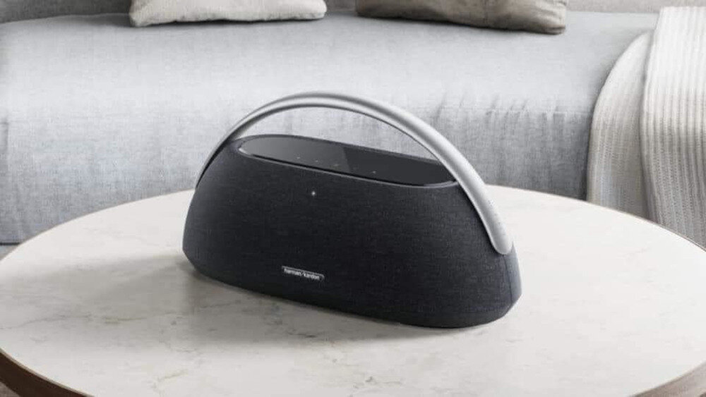 Na okrągłym stoliku znajduje się czarny głośnik z metalowym uchwytem. Na głośniku widoczne jest logo \'Harman Kardon\'.